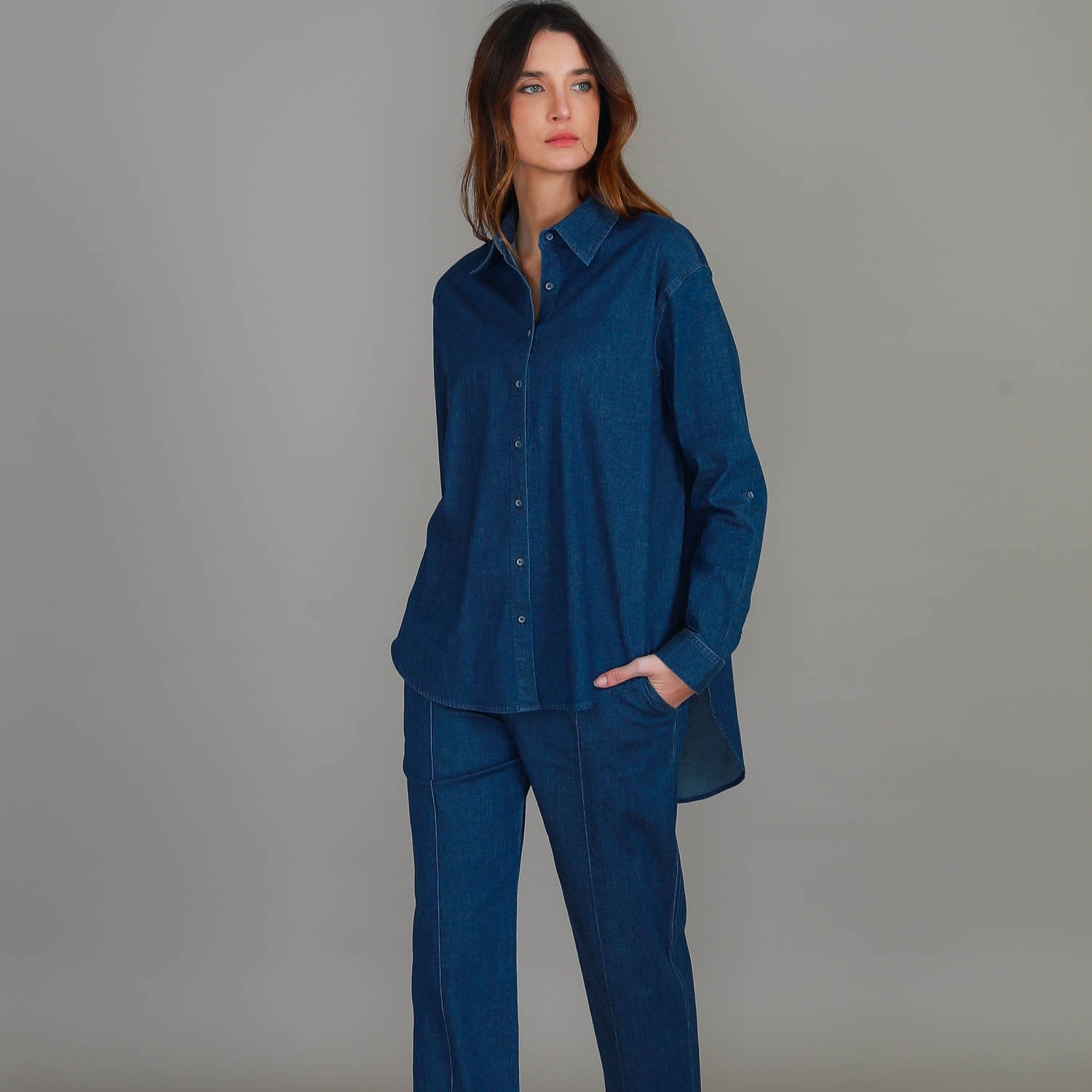 Woman wearing a blue shirt and pants against a gray background